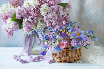 Spring still life with flowers, a bouquet of blooming lilacs and bird cherry in a vase, a basket...