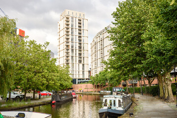 Modern apartment buildings along a canal lined with stone paths and trees on a cloudy summer day