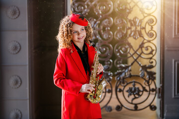 A young girl in a red coat and hat is holding a saxophone.