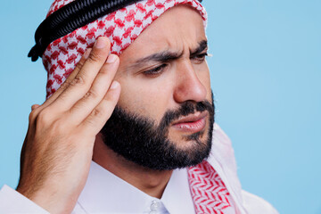 Muslim man rubbing temple and suffering from migraine symptom with tired expression. Arab person...