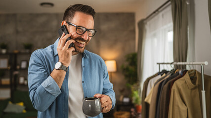 Portrait of adult man stand while talk on mobile phone and hold cup