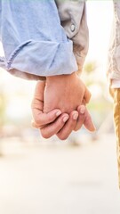 Beautiful close up photo of an unrecognizable caucasian couple holding hands outside against the sunlight. Copy space vertical image.
