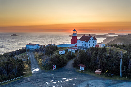 The sun is rising behind the Long Point Lighthouse illuminating the lens room at the top of the tower, Crow Head, Twillingate Island, Newfoundland