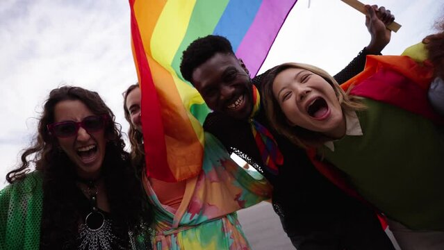 LGBT people shout excitedly looking at camera euphoric with a rainbow flag, capturing their fun and recreation very excited and enthusiastic. Gay and lesbian friends together at gay pride parade.