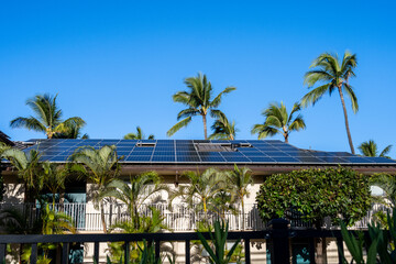 Condo building roof covered in solar panels to generate green alternative energy on sunny Maui, in contrast to the utility power distribution lines in front
