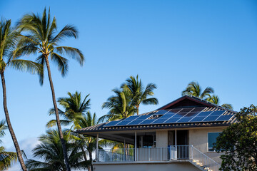 Fototapeta na wymiar Condo building roof covered in solar panels to generate green alternative energy on sunny Maui, in contrast to the utility power distribution lines in front 