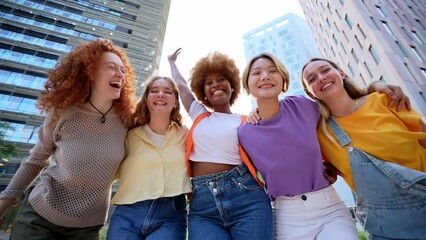 Multirracial cheerful young only women celebrating together. Excited cheerful female group looking at camera with skyscrapers at background having fun and laughing. Social gathering of diversity - Powered by Adobe