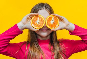 Little cute funny girl uses grapefruit for eyes and has fun in the studio on a yellow background....