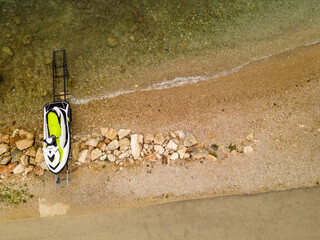 Obraz premium Aerial view of a jet ski parked on a rocky beach shoreline. The clear water and sandy beach create a perfect summer holiday vibe, ideal for adventure and water sports themes.