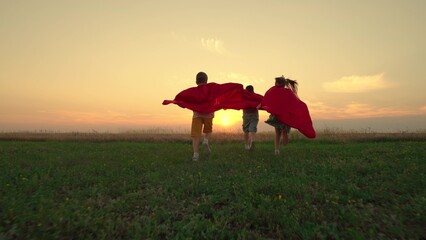 Boy, girl play red cape superhero, childhood dream. Child hero in red cloak running into sunset....