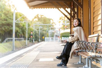 Asian woman listening to music with headphones and mobile phone app during waiting for train in the...