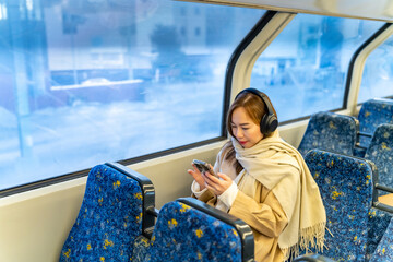 Asian woman using mobile phone and listening to the music on headphones during travel on train in...