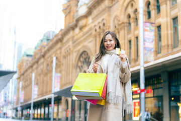 Asian woman holding credit card and shopping bag during shopping in the city. Attractive girl enjoy...