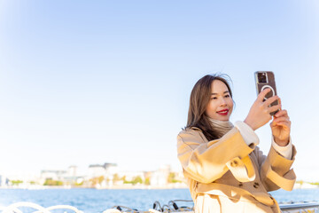 Asian woman using mobile phone taking selfie during travel on ferry boat crossing harbor in Sydney,...