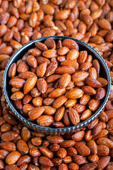 Roasted Almonds in a Decorative Bowl Close-Up Shot, A close-up image capturing roasted almonds filling an ornate bowl, with a multitude of nuts scattered around it, showcasing texture and color.