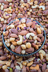 Assorted Nuts in a Decorative Bowl on Nut Background, An enticing close-up of a decorative bowl filled with an assortment of mixed nuts without skins, set against a blurred background of similar nuts.