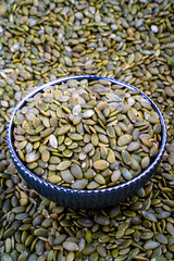 Bowl of Raw Sunflower Seeds on a Seed Background, Close-up view of a bowl filled with raw sunflower seeds, set against a background of scattered seeds.