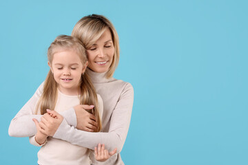 Mother hugging her happy daughter on light blue background. Space for text