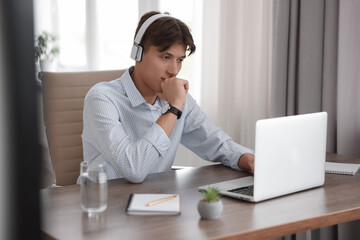 Fototapeta premium Man in headphones watching webinar at wooden table in office