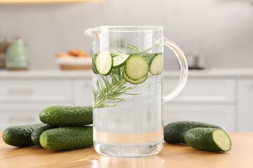 Refreshing cucumber water with rosemary in jug and vegetable on wooden table