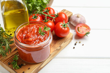 Homemade tomato sauce in jar and fresh ingredients on white wooden table, closeup