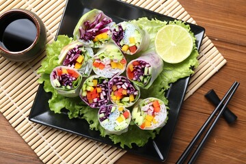 Delicious spring rolls, soy sauce and chopsticks on wooden table, top view