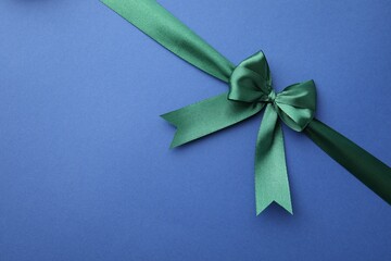 Green satin ribbon with bow on blue background, top view. Space for text