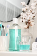 Bottle of mouthwash and glass on white table in bathroom