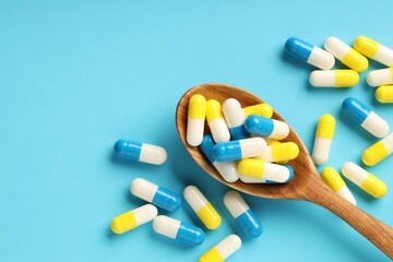 Many antibiotic pills with wooden spoon and space for text on light blue background, top view....