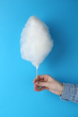 Woman holding sweet cotton candy on light blue background, closeup