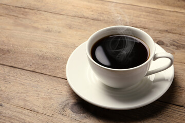 Steaming coffee in cup on wooden table. Space for text