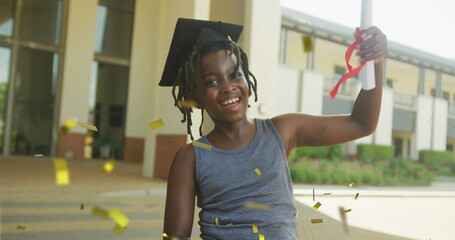 Image of gold confetti over happy african american schoolboy in mortar board holding diploma