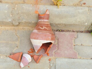 A broken earthen pitcher pot on the pavement, matki or matka used for water storage cooler, made by...