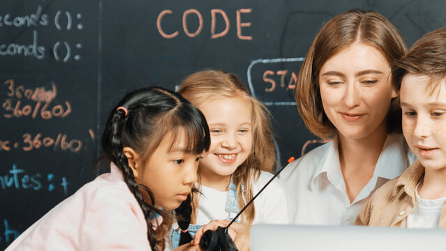 Smart teacher and diverse student looking at laptop on table with car model placed. Caucasian mentor inspect, explain, teaching engineering code or prompt in STEM technology classroom. Erudition.