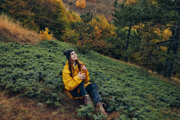 Woman in Yellow Jacket Sitting on Hillside with Autumn Trees in Background Enjoying Nature's Beauty...