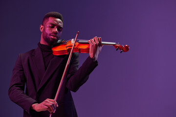 Elegant musician in black suit playing violin on a vibrant purple background for musical concept