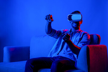 Happy man drive a car movement while wear VR glasses and sitting at sofa with neon light...