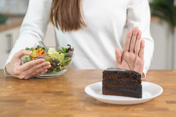 Diet, Dieting asian young woman using hand push out, deny chocolate cake or sweet taste, dessert food, choose eat green salad vegetables when hungry. Nutritionist of healthy, nutrition of weight loss.