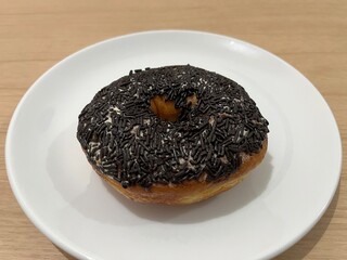 A single chocolate donut with sprinkles and butter on a white plate