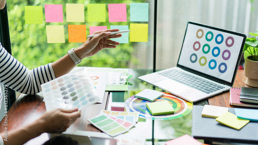 Poster creative graphic designer holding color swatch and comparing color on laptop for designing project
