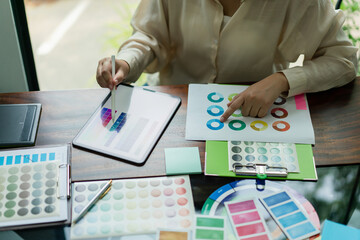 Creative graphic designer comparing color swatch on tablet and document for designing new project