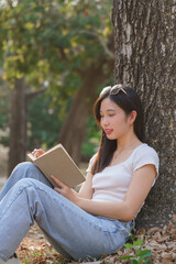 Young asian women sitting on grass to leaning the tree and reading a literature book with recreation happiness while enjoying to relaxation with journey travel trip lifestyle in the nature park