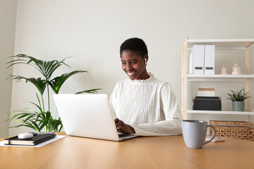 Black female entrepreneur working at home office. Happy African American woman using laptop and...