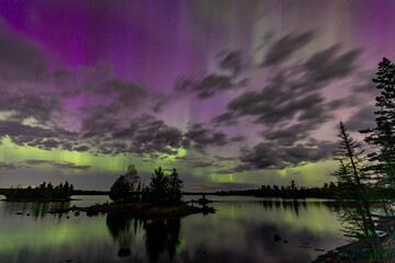 Northern lights erupt over a lake in Minnesota in a dark sky overhead shining rainbow of Aurora...