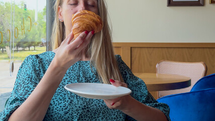 Portrait of attractive cute young woman enjoying tasty croissant in the cafe