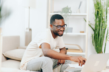 African American Man Working on Laptop in Modern Home Office, Smiling and Engaged in Online...