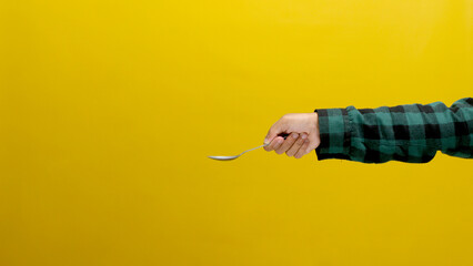 Hand Holding a Silver Stainless Steel Spoon, Isolated on a Yellow Background