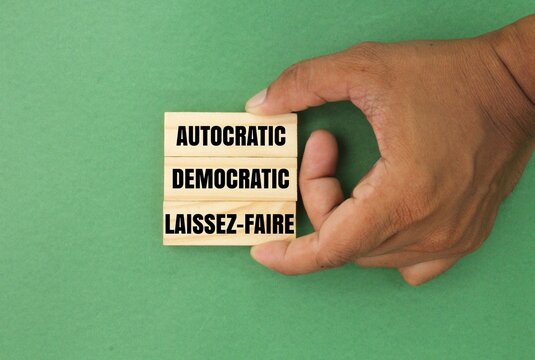 hand holding a stick with the three words of three main management styles, namely Autocratic, Democratic, and Laissez-Faire.