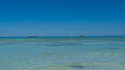 Minimalistic idyllic seascape. Transparent calm aquamarine ocean and clear blue sky. Tiny islands...