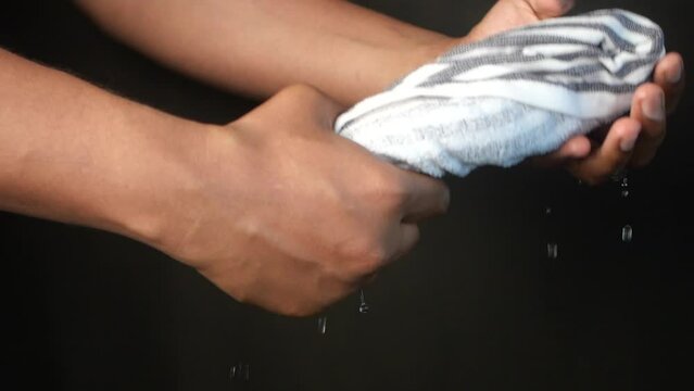 slow motion of Hands squeeze wet towel against black background. draining water from wet towel..